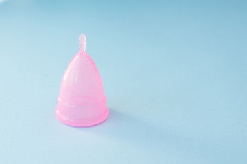 Pinc menstrual cup on blue background, copy space. close-up