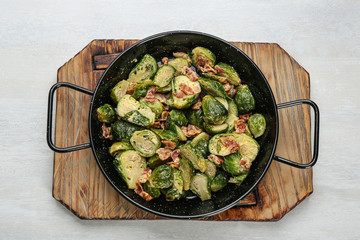 Delicious cooked Brussels sprouts with bacon in pan on white table, top view