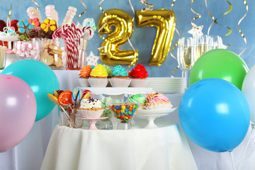 Dessert table in room decorated with golden balloons for 27 year birthday party