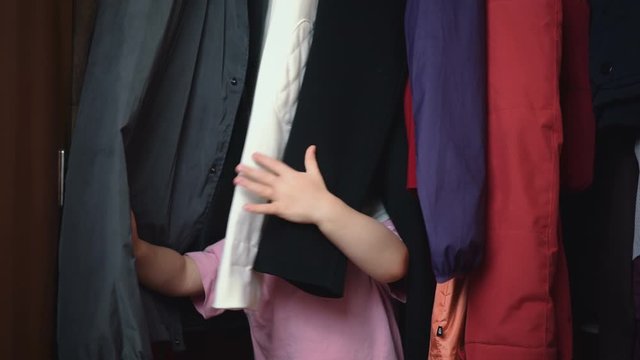 children play hide and seek at home. the child is hiding in the closet with clothes