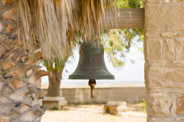 Ritual sacral bell outdoor in garden of a church, next to a palm tree.