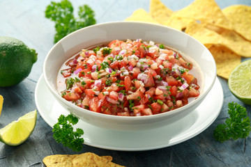 Mexican Tomato Salsa in white bowl with lime, red onion, jalapeno pepper, parsley and tortilla chips