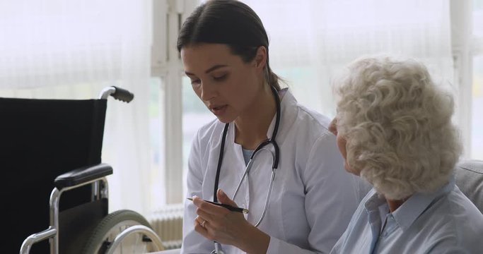 Young woman doctor consult disabled handicapped old grandma patient