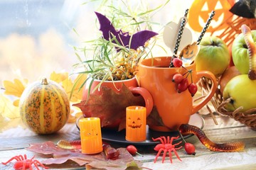 Obraz na płótnie Canvas Halloween decor, a couple of cups with a drink, decorative candles, pumpkins, berries, leaves on the windowsill, autumn seasonal holidays, the concept of home comfort