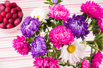 Red plums in pink bowl and  bouquet of chrysanthemums on  colorful striped tablecloth.