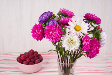 red fresh ripe plums on bowl and glass vase with a bouquet of chrysanthemums.  Vegetarian or healthy eating.