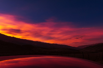 Fiery cloudy sunset over the mountains reflected on a car roof