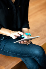 Close up photo of a woman using and working on her digital tablet computer sitting in the auditorium. Wearing a blue jeans and a watch. Mobile and technology app, portrait photography.