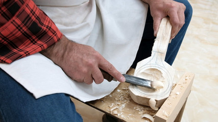 Traditional handicraft woodworking or hobby. An elderly man cuts a spoon out of a wooden block with...