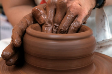 Female or male hands form a bowl on a spinning pottery wheel. Work with red clay. Traditional hand made dishes. Shallow depth of field. Selective focus. Copy space.