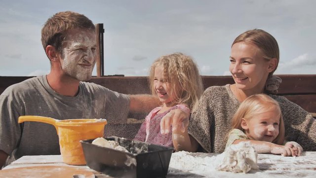The young family knead the dough for bread and throw flour at each other.
