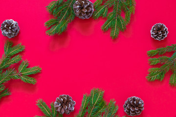 Fototapeta premium Christmas flat lay on red background with green pine branches and pine cones. Image with copy space, top view