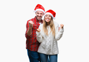 Young couple in love wearing christmas hat over isolated background very happy and excited doing winner gesture with arms raised, smiling and screaming for success. Celebration concept.