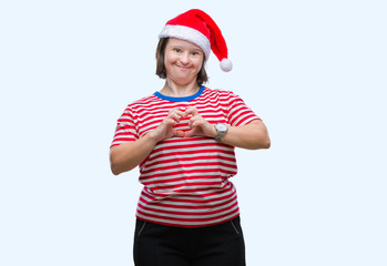 Young adult woman with down syndrome wearing christmas hat over isolated background smiling in love showing heart symbol and shape with hands. Romantic concept.
