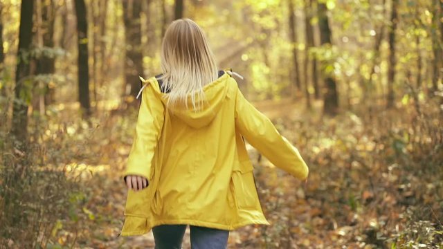 Smiling blonde woman having fun, running in the autumn forest. Turns around, looking at the camera and smiling. Slowmotion. Handheld shot.