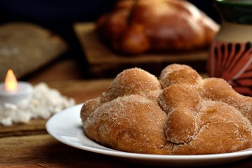 Mexican tradition, Bread of the dead made with butter and egg, on a wooden base, in the background a jug with coffee and a pan of the dead without sugar on top, adorned with a candle-style spotlight.