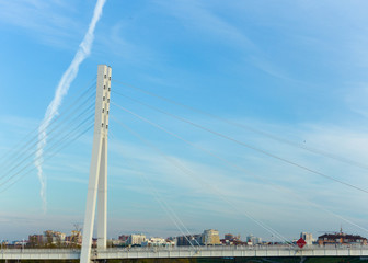 Fototapeta premium A pedestrian bridge with a supporting structure, a vertical tower with steel cables, against a light blue sky.