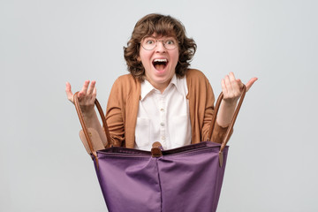 Young funny woman with big shopping bag being happy to find something inside, Studio shot
