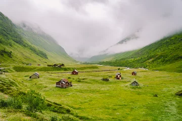 Fotobehang Beautiful landscape and scenery view of Norway, green scenery hills and mountain in a cloudy day. green scenery of hills and mountain partially covered with fog. Farm and cottages on a glacier river © Elizaveta