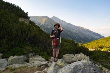 Young happy female with backpack and gas lantern stand in the beautiful mountains