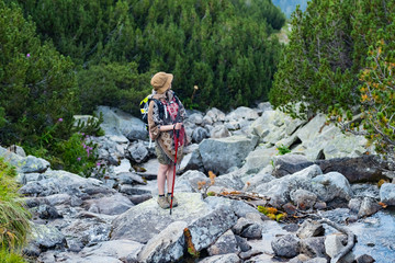 Naklejka na ściany i meble Young woman traveler in poncho and with backpack stand on the big rocks