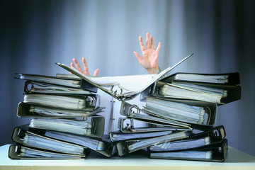 raised hands of a person who sinks behind stacks of ring binders on an office desk, concept of...