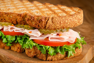 handmade tasty turkey sandwich with tomato, salad and cucumber, on wooden background, closeup