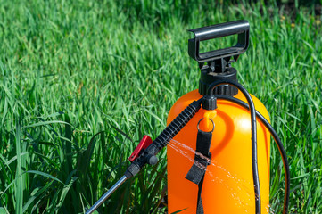 Jets of aqueous chemical solution gush from the black plastic handle of the orange sprayer....