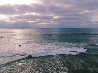 Aerial view of surfers waiting, paddling and enjoying waves before sunset time. Del Mar Beach, California, USA