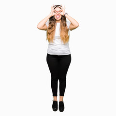 Fototapeta premium Young beautiful woman wearing casual white t-shirt doing ok gesture like binoculars sticking tongue out, eyes looking through fingers. Crazy expression.