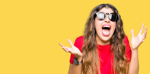 Young beautiful woman wearing red t-shirt and sunglasses celebrating mad and crazy for success with...