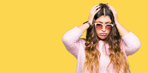 Young beautiful woman wearing sunglasses and pink sweater suffering from headache desperate and stressed because pain and migraine. Hands on head.