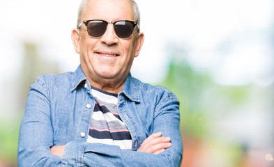 Obraz premium Handsome senior man wearing denim jacket and sunglasses happy face smiling with crossed arms looking at the camera. Positive person.