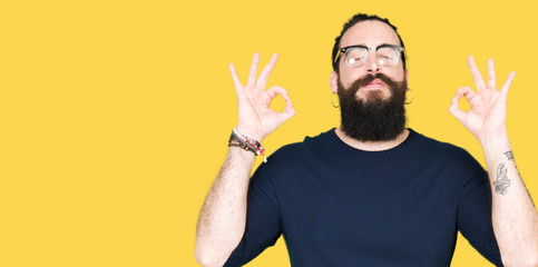 Young hipster man with long hair and beard wearing glasses relax and smiling with eyes closed doing meditation gesture with fingers. Yoga concept.