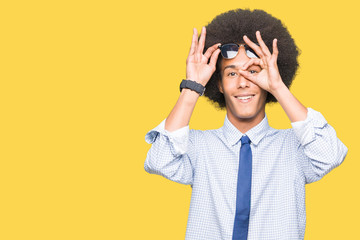 Young african american business man with afro hair wearing sunglasses doing ok gesture with hand smiling, eye looking through fingers with happy face.