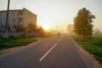 Morning fog with the rising sun on the street in the village .