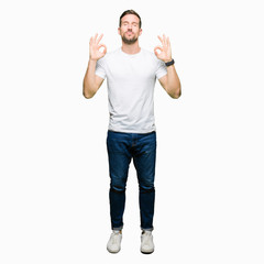 Handsome man wearing casual white t-shirt relax and smiling with eyes closed doing meditation gesture with fingers. Yoga concept.