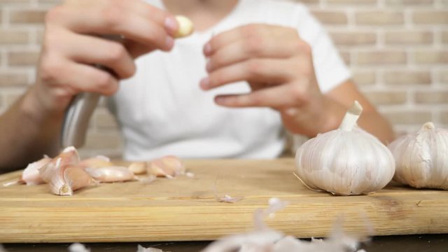 closeup head of garlic, male hands peel the garlic on a wooden board