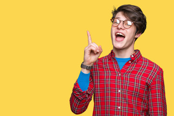 Young handsome man wearing glasses over isolated background pointing finger up with successful idea. Exited and happy. Number one.