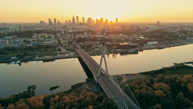 Establishing Aerial Panoramic Shot of Warsaw Cityscape, capital of Poland. Swietokrzyski Suspension Bridge and Urban Downtown Skyline at Sunset. 4K Tilt Background Drone Bird's-eye view Video