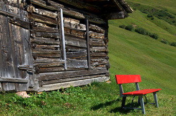 Red bench in front of a wooden house in the Alps