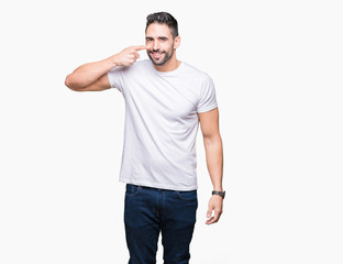 Handsome man wearing white t-shirt over white isolated background Pointing with hand finger to face and nose, smiling cheerful