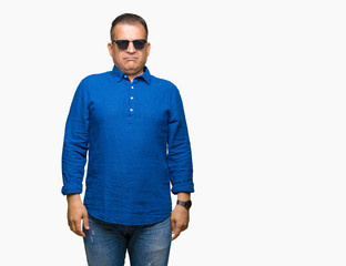 Middle age arab man wearing sunglasses over isolated background with serious expression on face. Simple and natural looking at the camera.