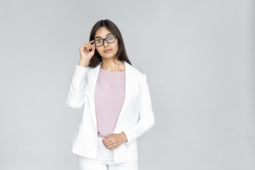 Confident serious smart young adult indian business lady in formal wear suit standing isolated on grey background with copy space. Successful woman looking at camera through eyewear