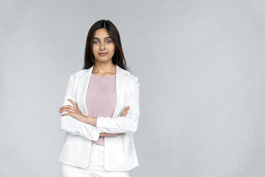 Confident and successful young adult indian businesswoman in white suit crossed arms on chest, standing isolated on grey background with copy space and looking at camera