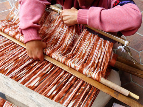 Close up man's arms wprking on traditional weaving technique Ikat for making scarfs or Macana or other fabric by hand with cotton threads, design are traditional for Gualaceo, Azuay province, Ecuador