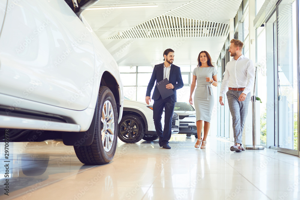 Wall mural couple and the dealer selling cars look the car in the showroom.