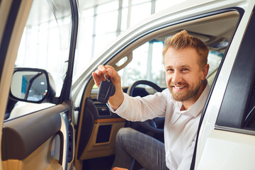 Auto buyer man with keys in hand in a new car in auto salon.