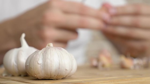 closeup head of garlic, male hands peel the garlic on a wooden board