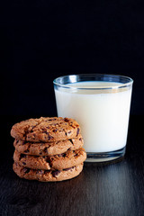 COOKIES WITH CHOCOLATE CHIPS AND MILK GLASS ON BLACK BACKGROUND